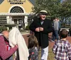 A group of people is listening to a woman dressed in historical attire possibly a reenactor or tour guide on a street that appears to come from an earlier era