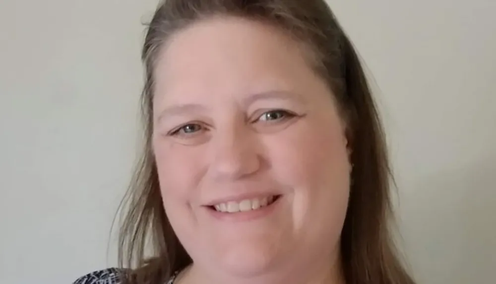 A smiling woman with shoulder-length hair is posing for a headshot in front of a plain background