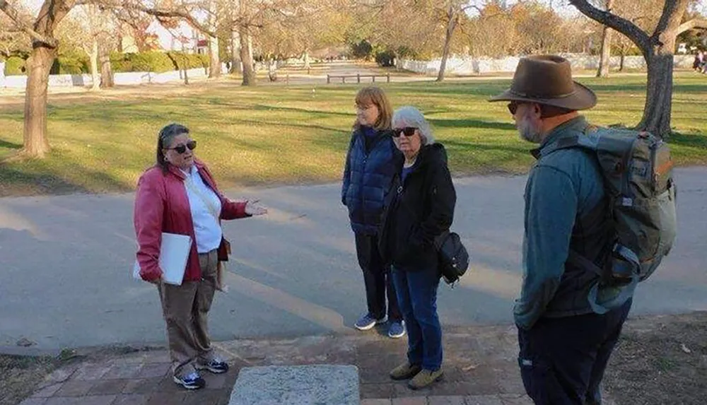 A person is gesturing while talking to a group in a park-like setting