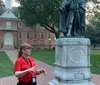 A person is giving a tour or presentation next to a statue with a historical building in the background