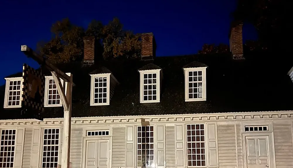 The image shows an old-fashioned house at night illuminated from below with a dark blue sky in the background and a traditional signpost by its side