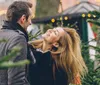 A happy couple is sharing a joyous moment together amidst a setting of evergreen trees likely representing a festive or holiday atmosphere