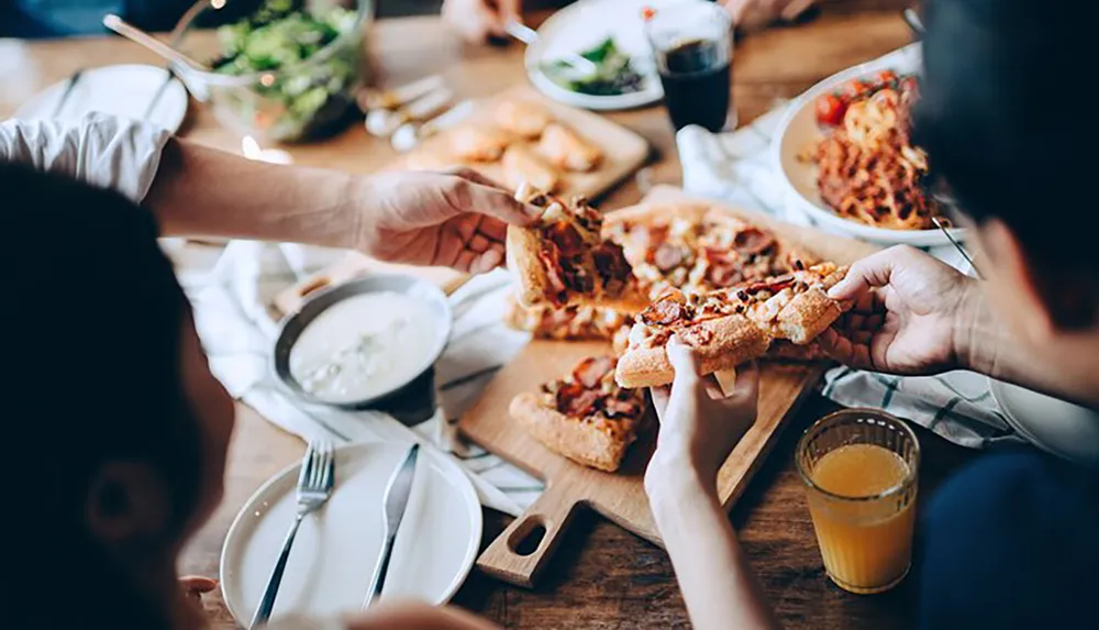 A group of people is enjoying a meal together sharing a pizza and other dishes on a wooden table