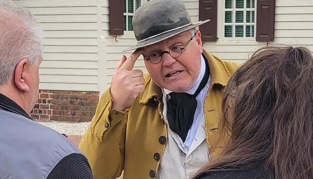 A man in historical costume is engaging in conversation with two individuals gesturing to his head as if explaining a point