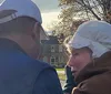 Two people dressed in historical military costumes are participating in an outdoor community event with a crowd that includes children playing