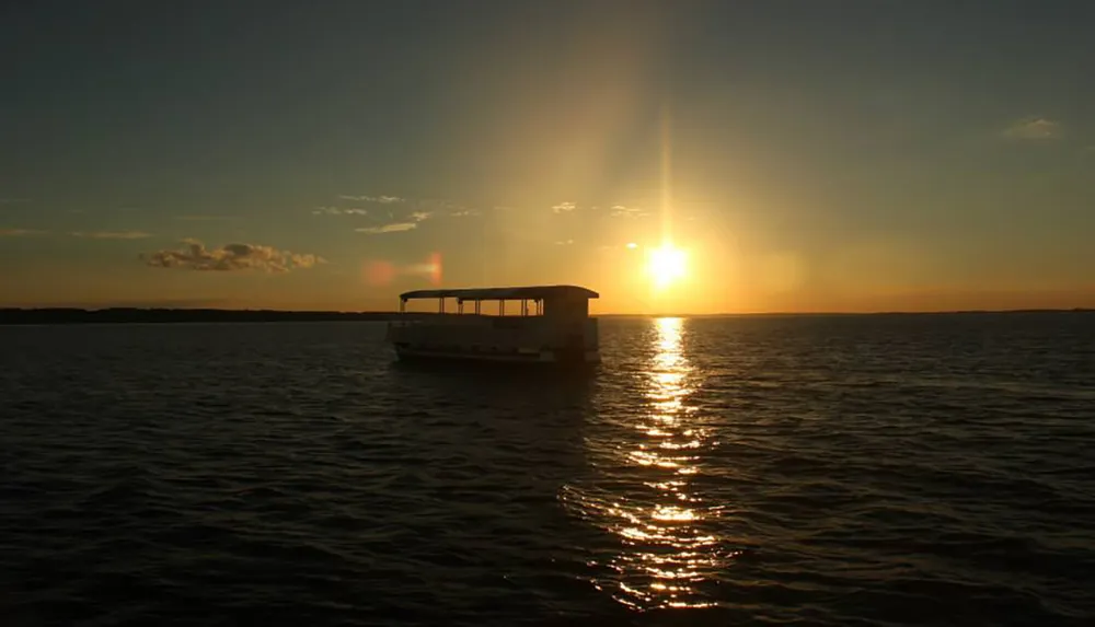 A boat is silhouetted against a vibrant sunset over calm waters