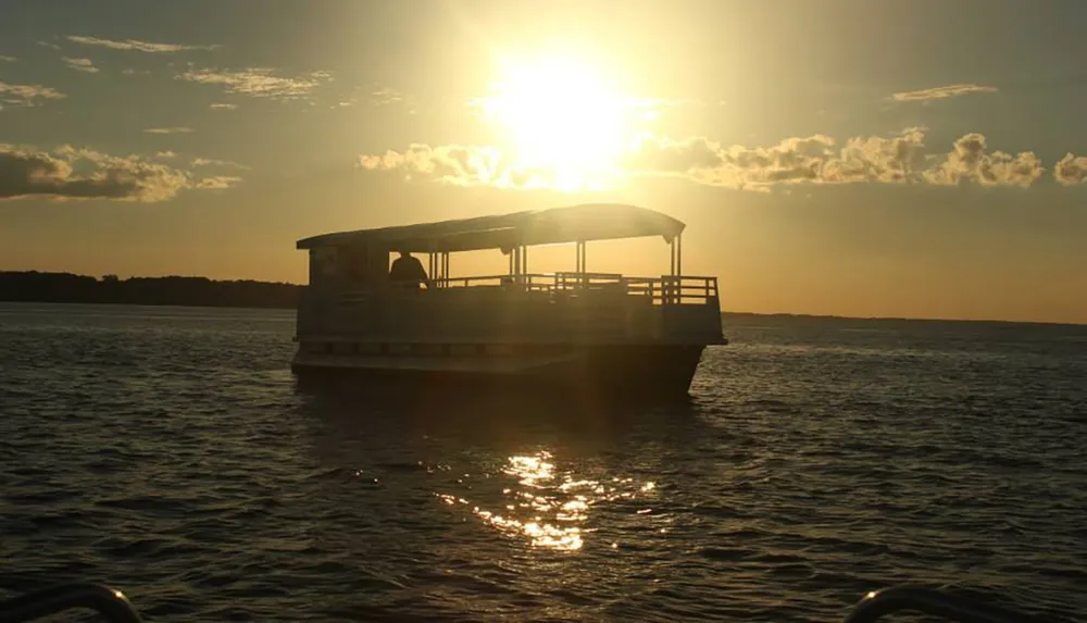 A boat is silhouetted against a bright sunset over a calm body of water