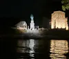 The image shows a nighttime scene with a brightly lit monument and a historic building reflecting on a body of water