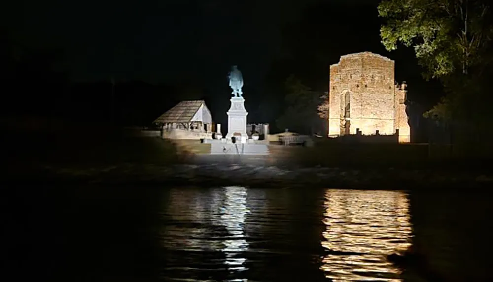 The image shows a nighttime scene with a brightly lit monument and a historic building reflecting on a body of water