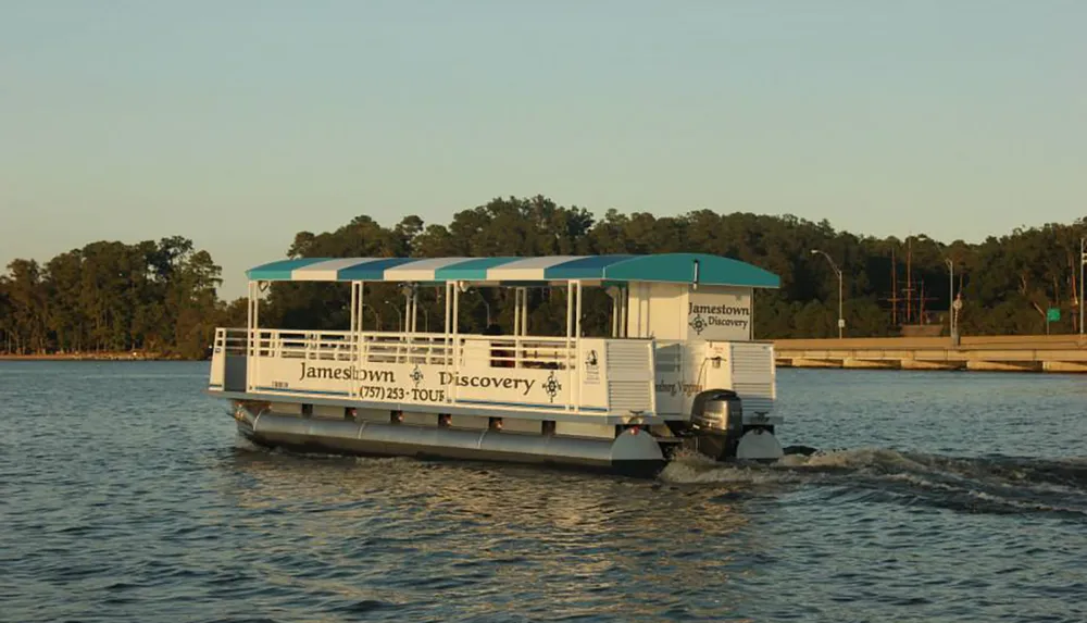 A tour boat named Jamestown Discovery travels on tranquil water near a wooded shoreline