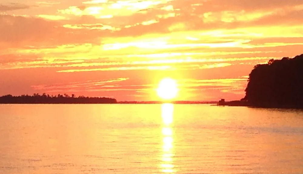 A vibrant sunset over a calm body of water with silhouetted landmasses on either side