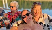 Three women are smiling and enjoying a sunny day on a boat with drinks.