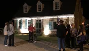 A group of people is gathered outside of a historical building at night, possibly on a guided tour.