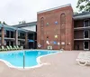 A swimming pool is surrounded by a brick building with colorful star decorations green chairs and white lounge chairs on the deck