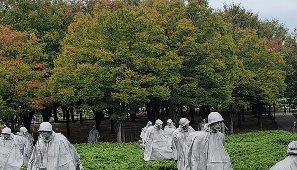 Statues depicting a group of soldiers stand amidst greenery with a backdrop of trees showing early autumn colors