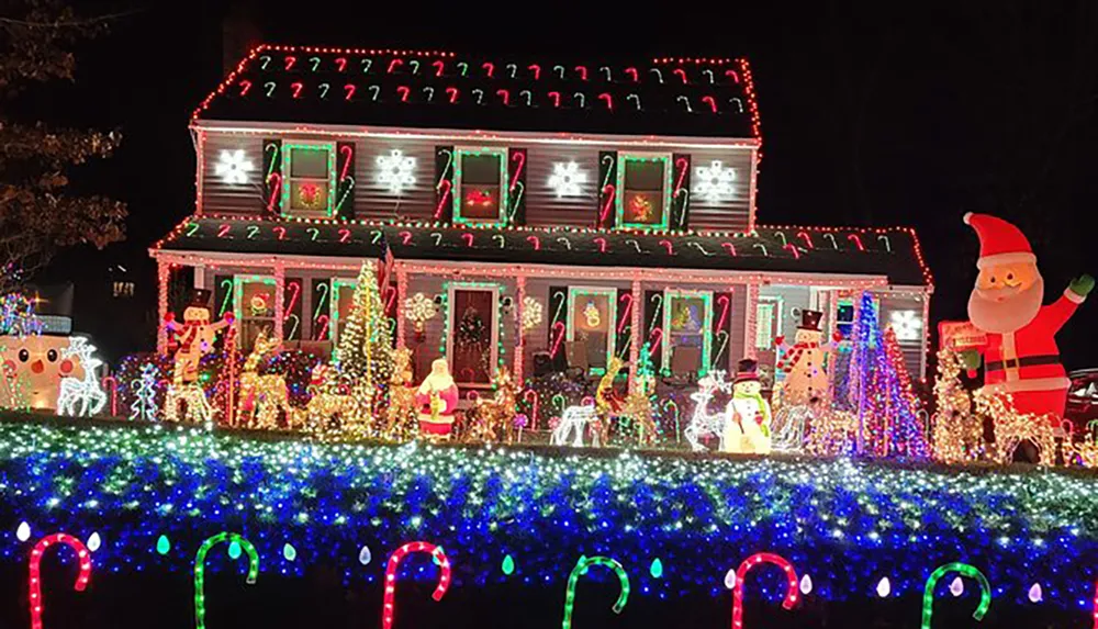 The image shows a house elaborately decorated with colorful Christmas lights festive ornaments and inflatable figures creating a vibrant holiday display at nighttime