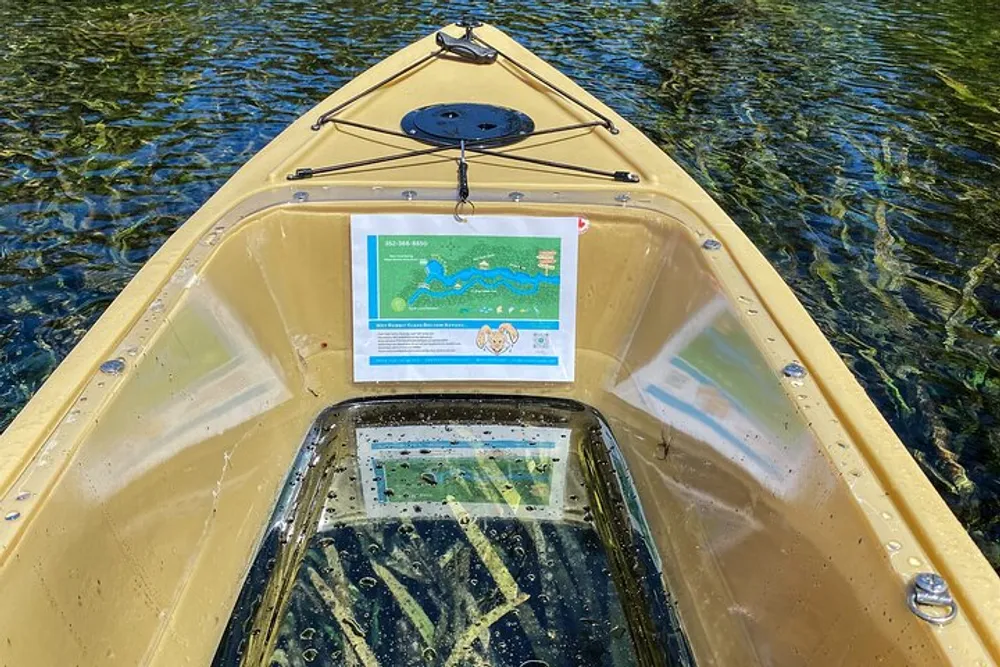 A yellow kayak with a transparent bottom and a map attached to the front is on clear water revealing aquatic plants below