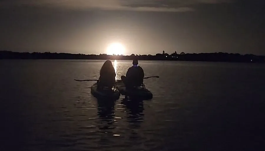 Two individuals are kayaking on a calm body of water against the backdrop of a beautiful sunset.