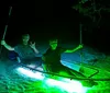 Two people are enjoying a nighttime adventure in a transparent kayak illuminated by a green light highlighting the water below them