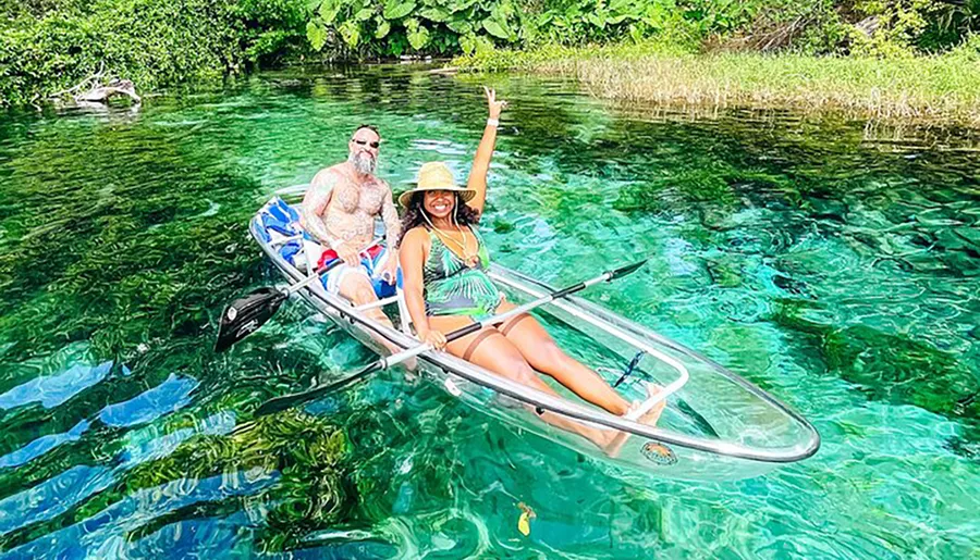 A couple is enjoying a sunny day kayaking on a clear, emerald green waterway surrounded by lush greenery.