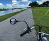 A bicycle with a basket and rear cargo rack is parked on the grass by a coastal roadway with a view of the water and clear sky in the background