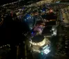 The image shows a nighttime aerial view of a vibrant illuminated cityscape with a bridge crossing a body of water and fireworks bursting in the distance