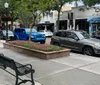 The photo captures a peaceful street view showcasing parked cars a vibrant blue Jeep a sitting area with a bench and a tree-lined sidewalk in an urban setting