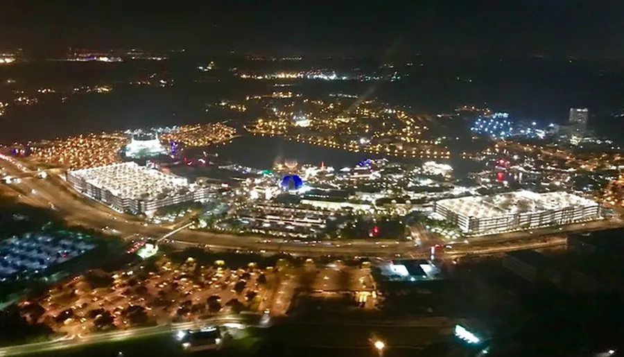 An aerial nighttime view shows a brightly lit urban area with dense buildings, roads, and various sources of illumination.