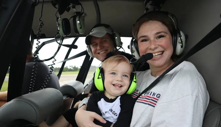 A family of three is smiling inside a helicopter, each wearing headsets, suggesting they are about to experience a flight together.