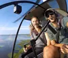 A man and a woman are smiling and taking a selfie inside a helicopter cockpit high above a landscape of water and greenery