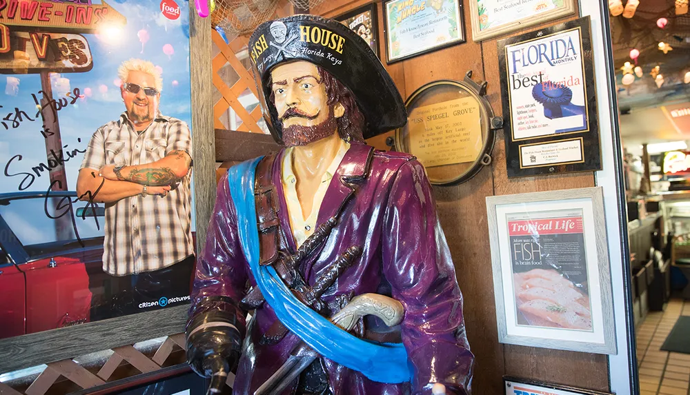 A life-size pirate statue stands in front of a wall adorned with celebrity photographs awards and magazine articles inside a restaurant