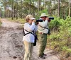 Two people equipped with cameras and binoculars are observing wildlife in a forested area