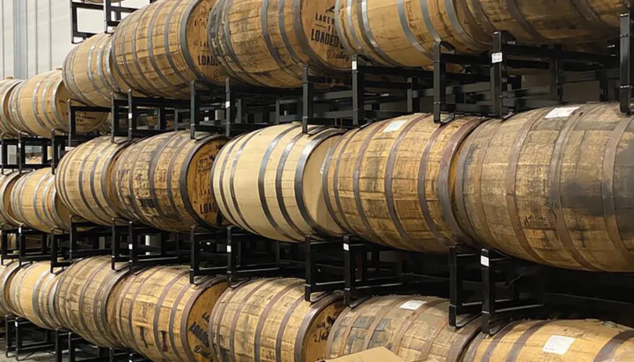 Multiple wooden barrels are neatly stacked on metal racks in what appears to be a distillery or aging warehouse.