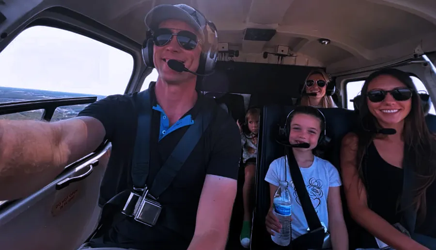 A group of individuals, presumably a family, is taking a selfie inside a helicopter, with everyone wearing headsets and some smiling at the camera.
