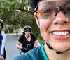 Three people are enjoying a bicycle ride on a scenic path with the person in the foreground taking a selfie and the other two waving and smiling behind her