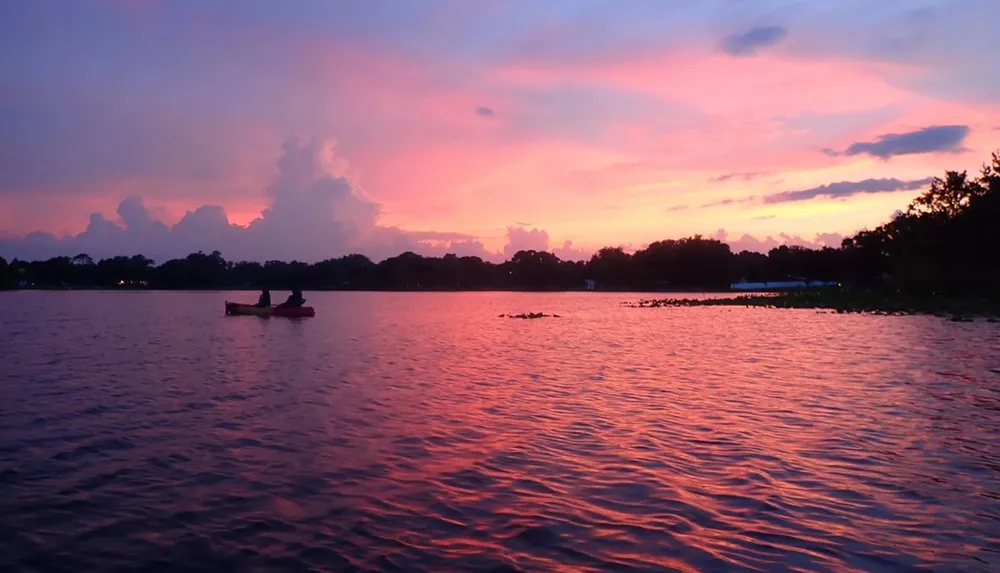 A person kayaks on tranquil waters under a stunning purple and orange sunset sky