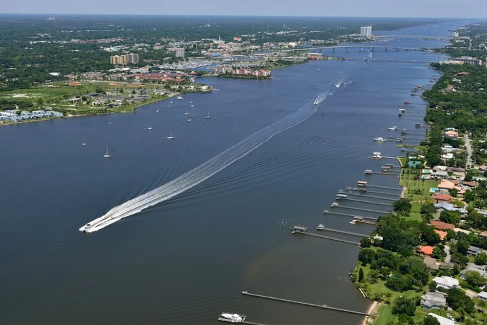 The image shows an aerial view of a wide river with a variety of boats and a cityscape in the background creating a lively scene of waterway transportation and urban life