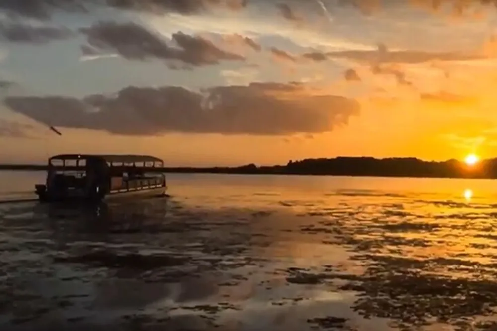 A boat glides across calm waters under a captivating sunset with hues of orange and yellow painting the sky