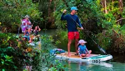 A group of people is enjoying paddleboarding and kayaking along a serene, forest-lined waterway.