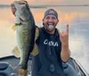 A smiling person is proudly holding a large fish on a boat with a body of water and a partly cloudy sky in the background