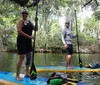 Two people are standing on paddleboards surrounded by tranquil waters and draped Spanish moss in a serene natural setting