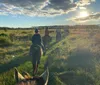 A group of horseback riders travels along a grassy trail at sunset