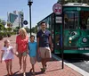 A family walks hand in hand on a sunny day next to a green trolley showing a sign that reads Out of Service