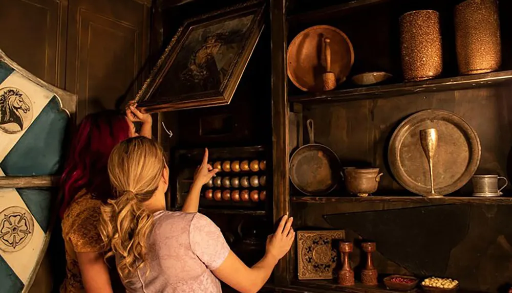 Two individuals are looking at or searching for something in a dark rustic cupboard filled with antique objects and crockery