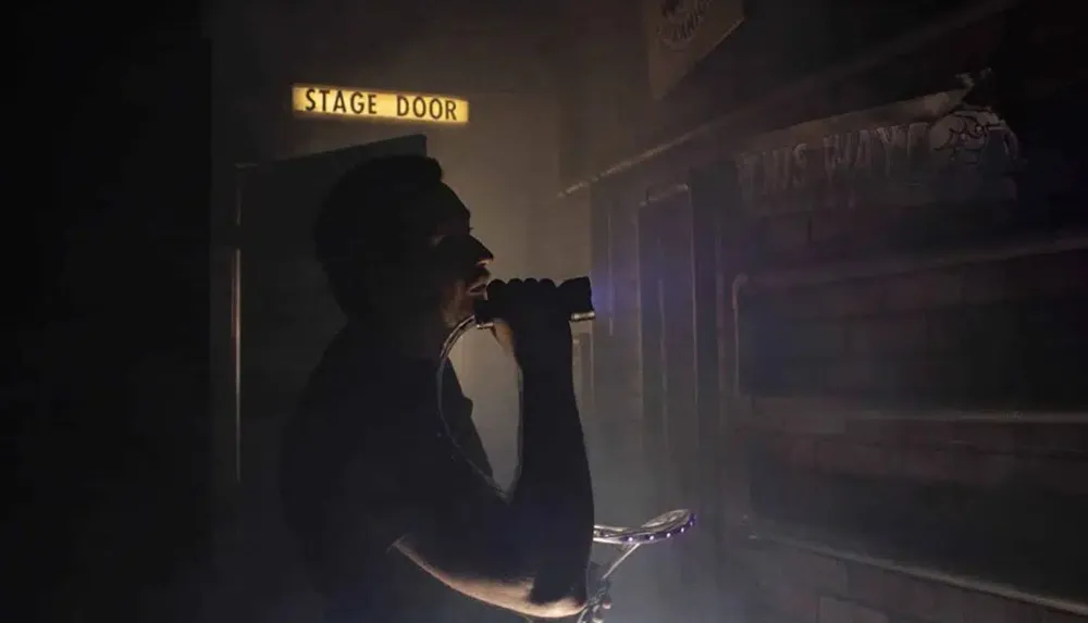 A person is silhouetted against a hazy and dimly lit backdrop with the words STAGE DOOR illuminated above suggesting a mysterious scene near the entrance of a performance venue