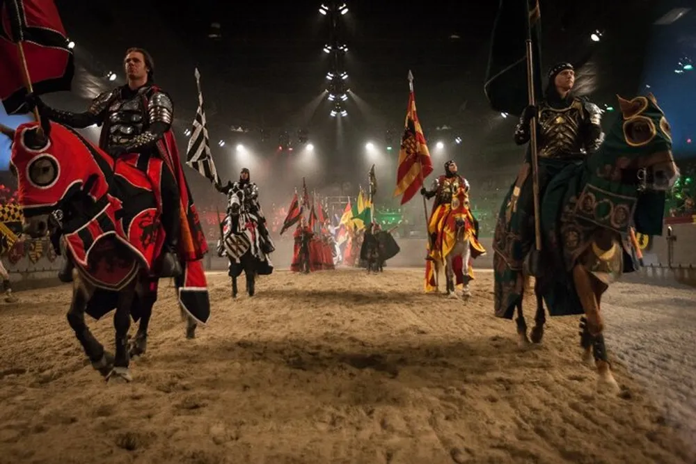 Knights on horseback and squires parade in a sandy arena with colorful medieval banners in the background evoking the ambiance of a chivalric tournament