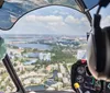 Two people are piloting a helicopter over a scenic coastal area with a clear view of the landscape and waterways below