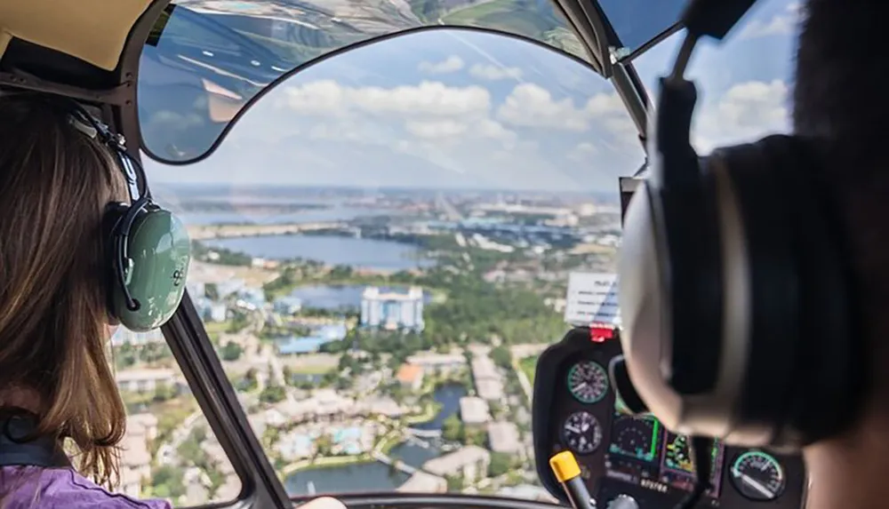 Two people are piloting a helicopter over a scenic coastal area with a clear view of the landscape and waterways below