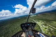 The image shows the cockpit view from a helicopter overlooking a lush landscape with roads and trees, taken from a high vantage point mid-flight.