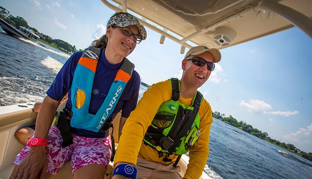 Two people are smiling and enjoying a sunny boat ride both wearing life jackets and sunglasses